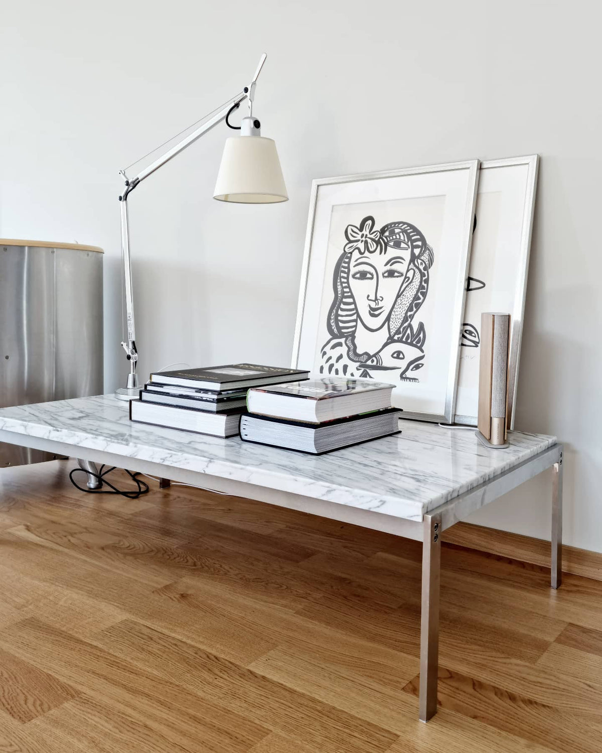 Clérachic floor lamp leaning in over a marble coffee table stacked with books and a framed line drawing.