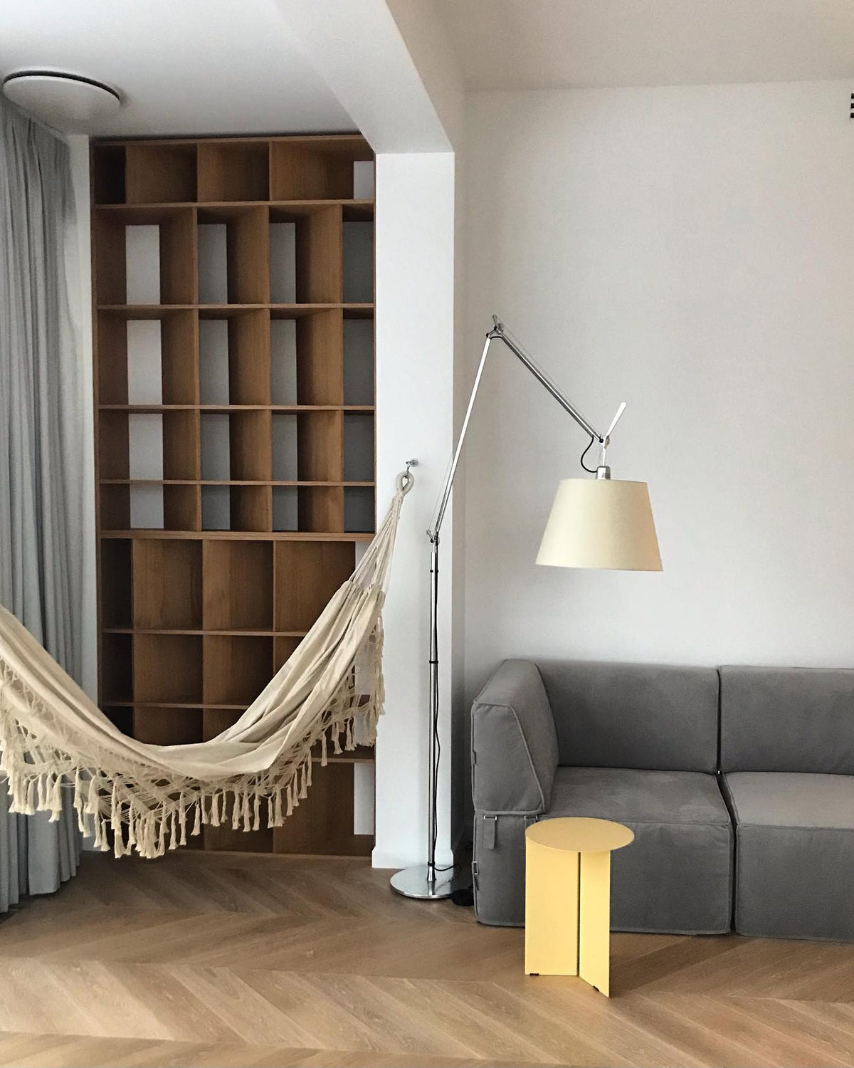 Clérachic floor lamp with a cream shade in a reading nook with a woven hammock, a grey sofa and a small yellow side table.