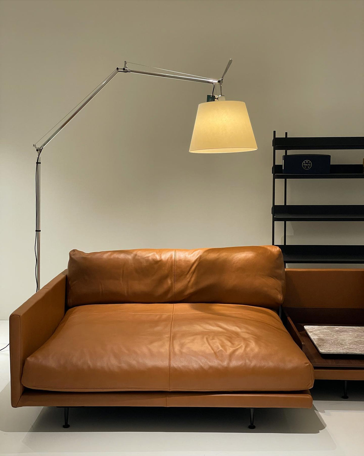 Lit Clérachic floor lamp with a warm cream shade, arched over a tan leather chaise in a pale room.