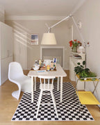 Clérachic floor lamp arm stretches above a white dining table with a black-and-white checked rug and a white moulded chair.