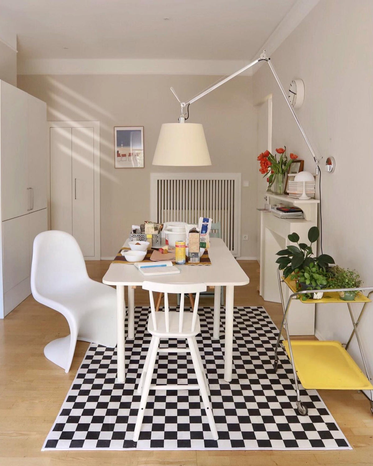 Clérachic floor lamp arm stretches above a white dining table with a black-and-white checked rug and a white moulded chair.