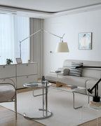 Clérachic arc floor lamp in a white living room with a pale sofa, a glass side table and low white cabinets.