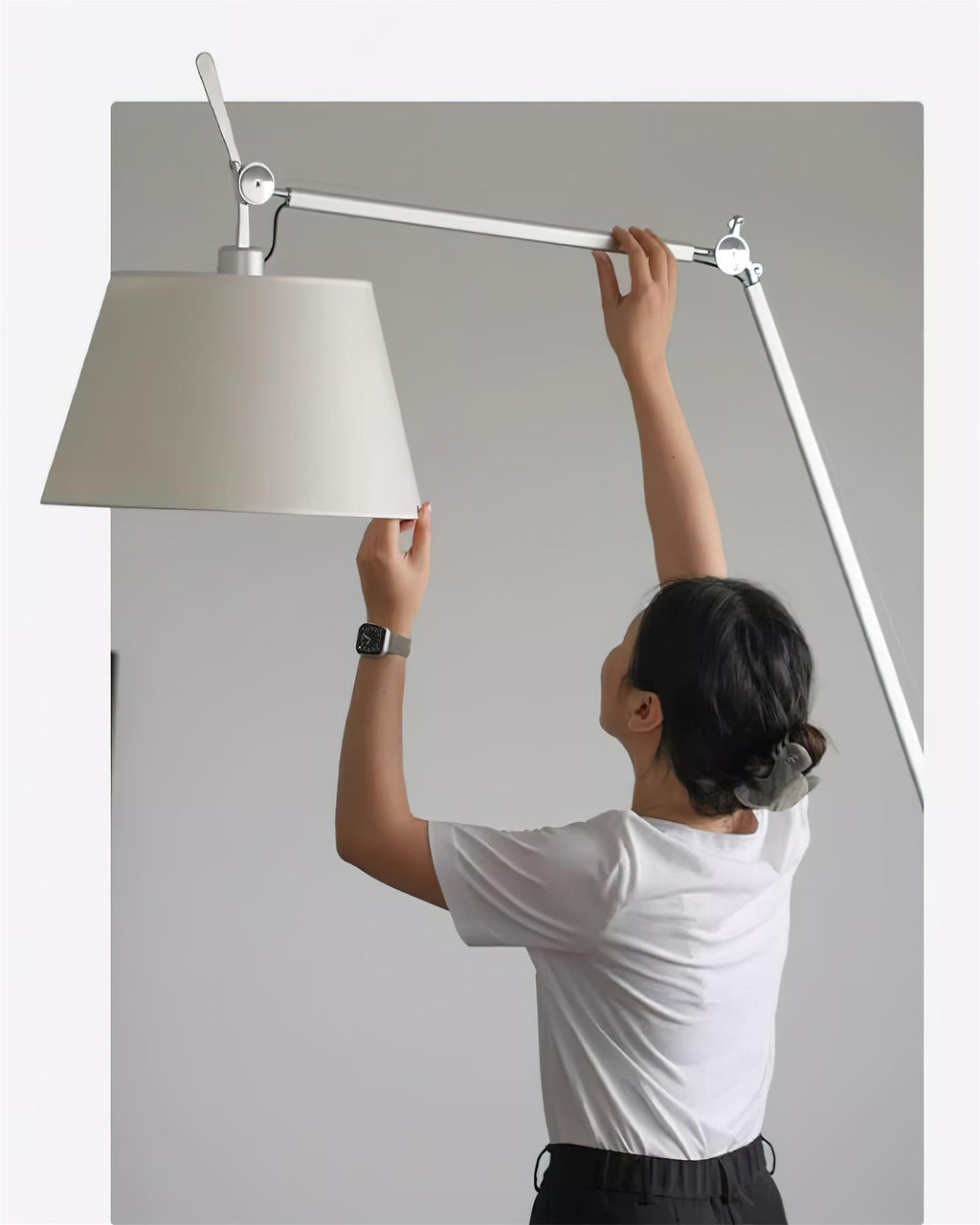 A person lifts the shade and adjusts the silver arm of this Clérachic floor lamp to aim it.