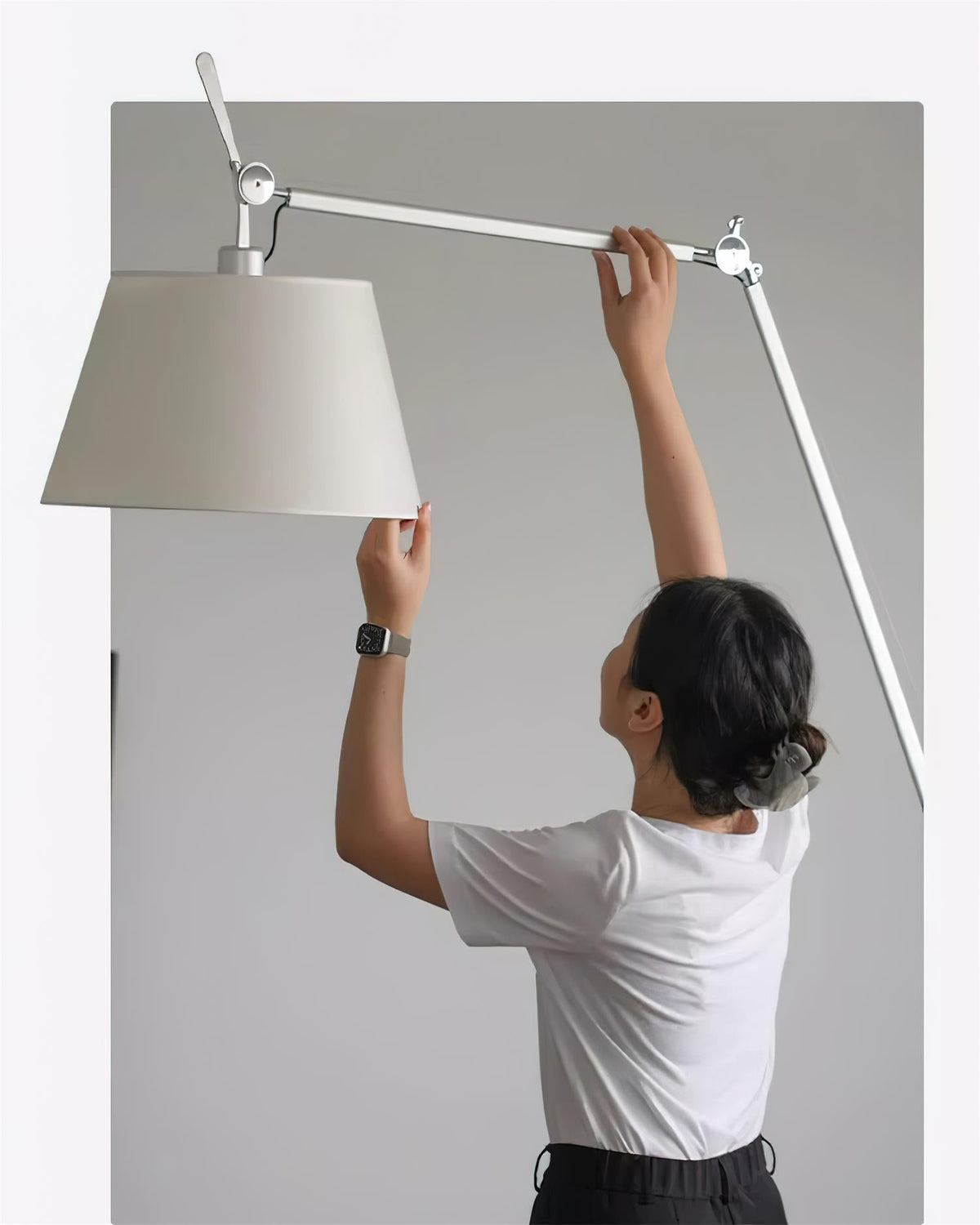A person lifts the shade and adjusts the silver arm of this Clérachic floor lamp to aim it.