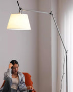 Closer view of a woman in an orange armchair beside this Clérachic floor lamp, its lit cream shade glowing above her.