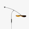 This Clérachic wall light on a plain white backdrop, its black arm curving out to a flat shade with a gold underside and a round bulb.