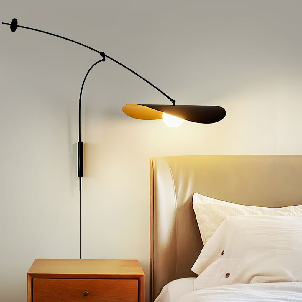 Lit beside a bed with a tan leather headboard and a wooden nightstand, this Clérachic wall light casts a warm glow from its black shade.