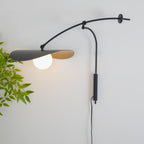 Close crop of this Clérachic wall light against a pale wall, a frosted white globe glowing under the black shade with green leaves beside it.