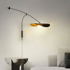 A Clérachic wall light glows beside a sculptural stone side table and a pale sofa, its black arm reaching across a soft grey wall.
