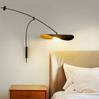 Beside a tan headboard and white pillows, this Clérachic wall light shines softly from a black shade lined in gold.