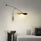 A Clérachic wall light on a plain wall with a stone side table and a grey sofa below, the shade glowing gently.