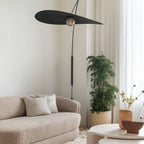 Raised high on its arm, this Clérachic wall light tilts a wide black shade above a boucle sofa and a potted tree.