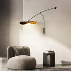 Beside a corner of cream wall, this Clérachic wall light lights an armchair and a small dark table with soft sunlight on the wall.