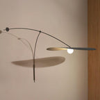 A Clérachic wall light with a long shadow on a warm beige wall, the black shade held flat beside a wooden panel.