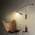 Beside a tan leather butterfly chair, this Clérachic wall light lights a dark textured wall with a glowing round bulb.
