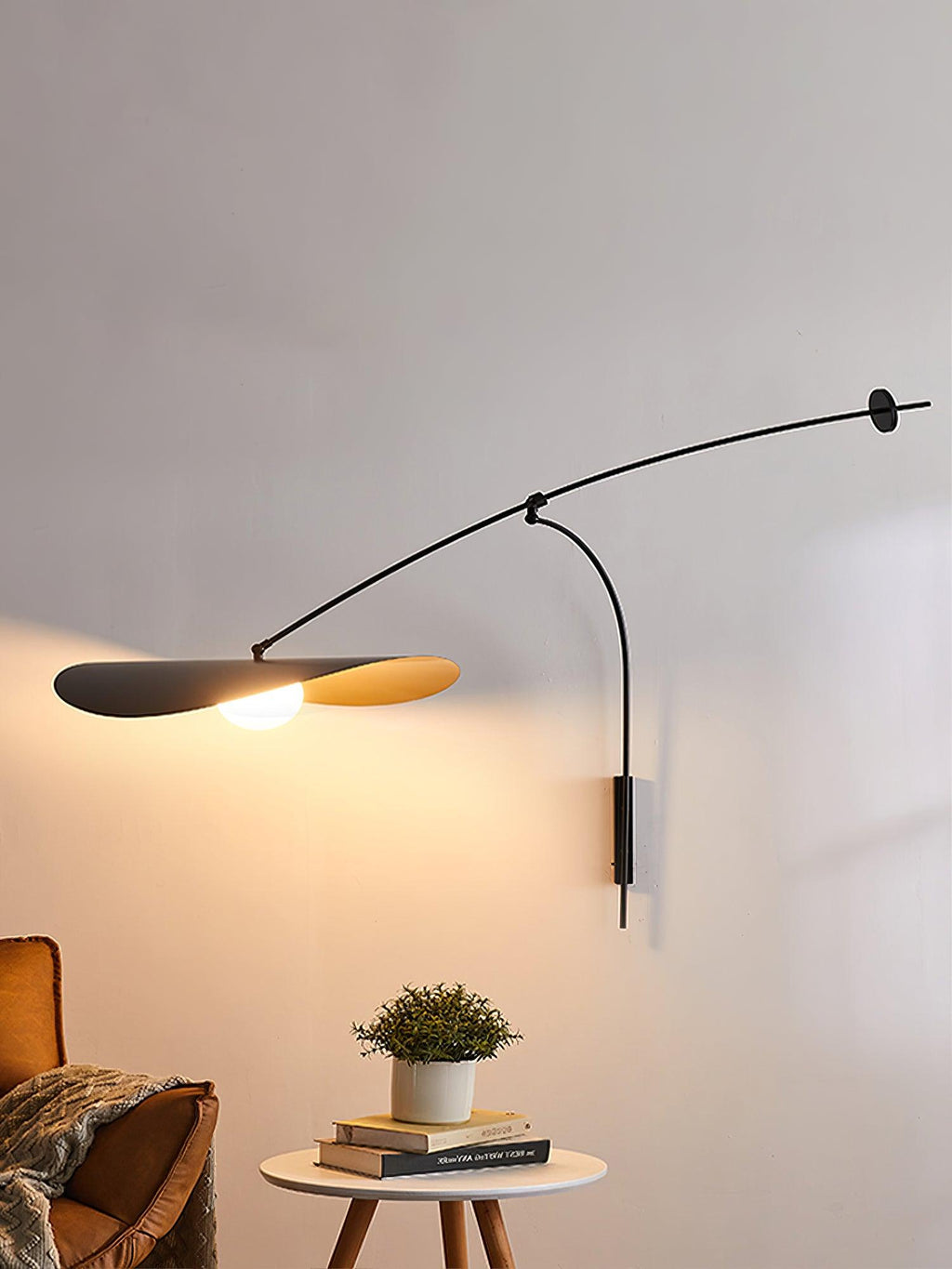 This Clérachic wall light lights a plant on a round side table, with a leather armchair at the left edge.