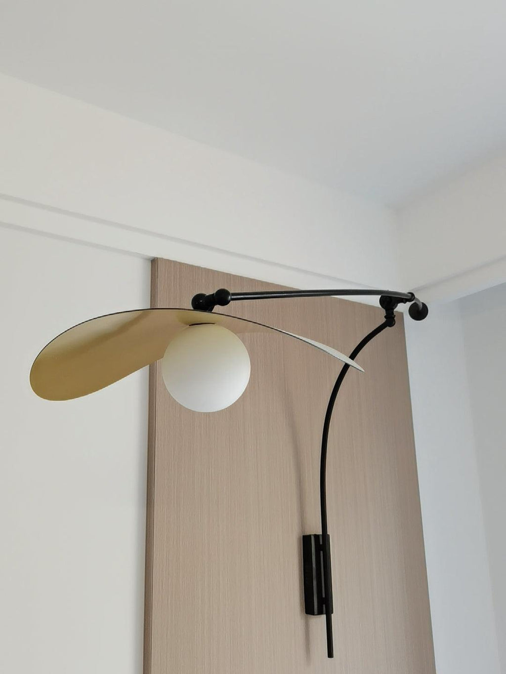 Looking up at this Clérachic wall light on an oak-veneer panel, the gold-lined shade tipped upward over a white globe.