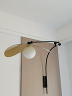 Looking up at this Clérachic wall light on an oak-veneer panel, the gold-lined shade tipped upward over a white globe.