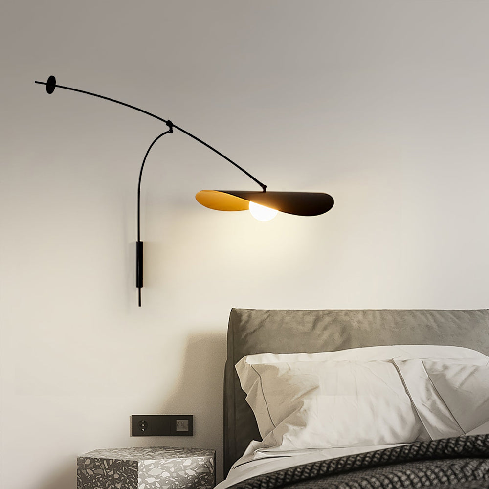 A Clérachic wall light glowing above a grey headboard and a terrazzo-style side table, with a wall switch plate beside it.