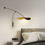 A Clérachic wall light glowing above a grey headboard and a terrazzo-style side table, with a wall switch plate beside it.