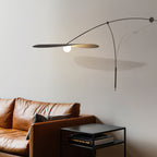 In a wide view, this Clérachic wall light leaves a long shadow on the wall behind a brown leather sofa.