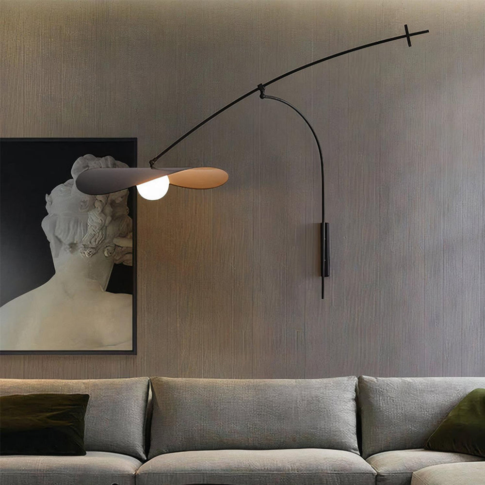 Lit above a grey sofa with green cushions, this Clérachic wall light sits beside a framed bust on a grey wall.