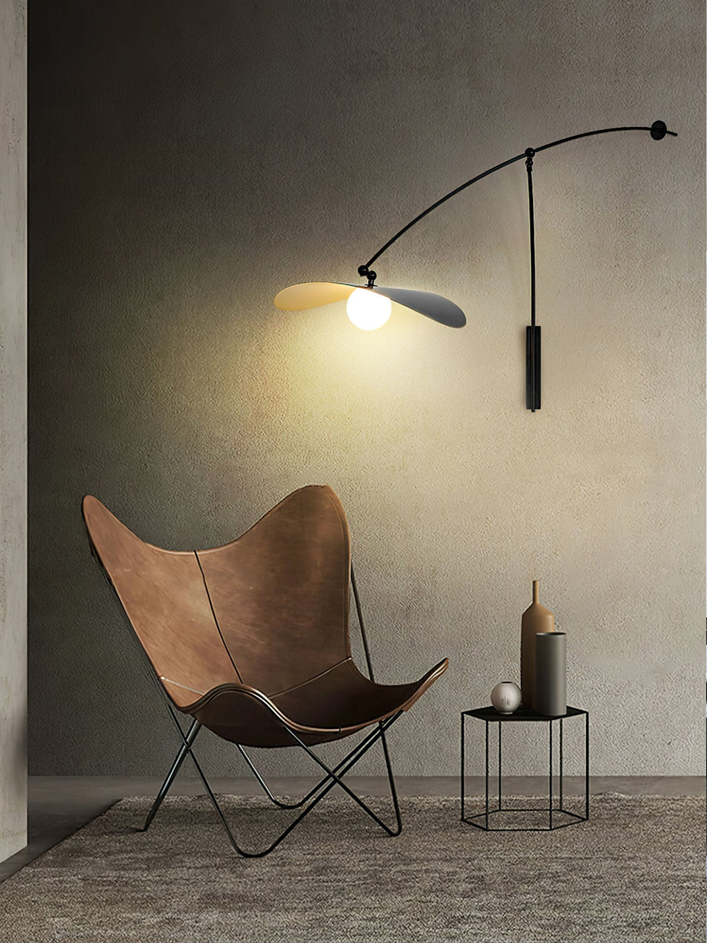 Tall photo of a Clérachic wall light on a dark wall, glowing above a brown butterfly chair and a hexagonal side table.
