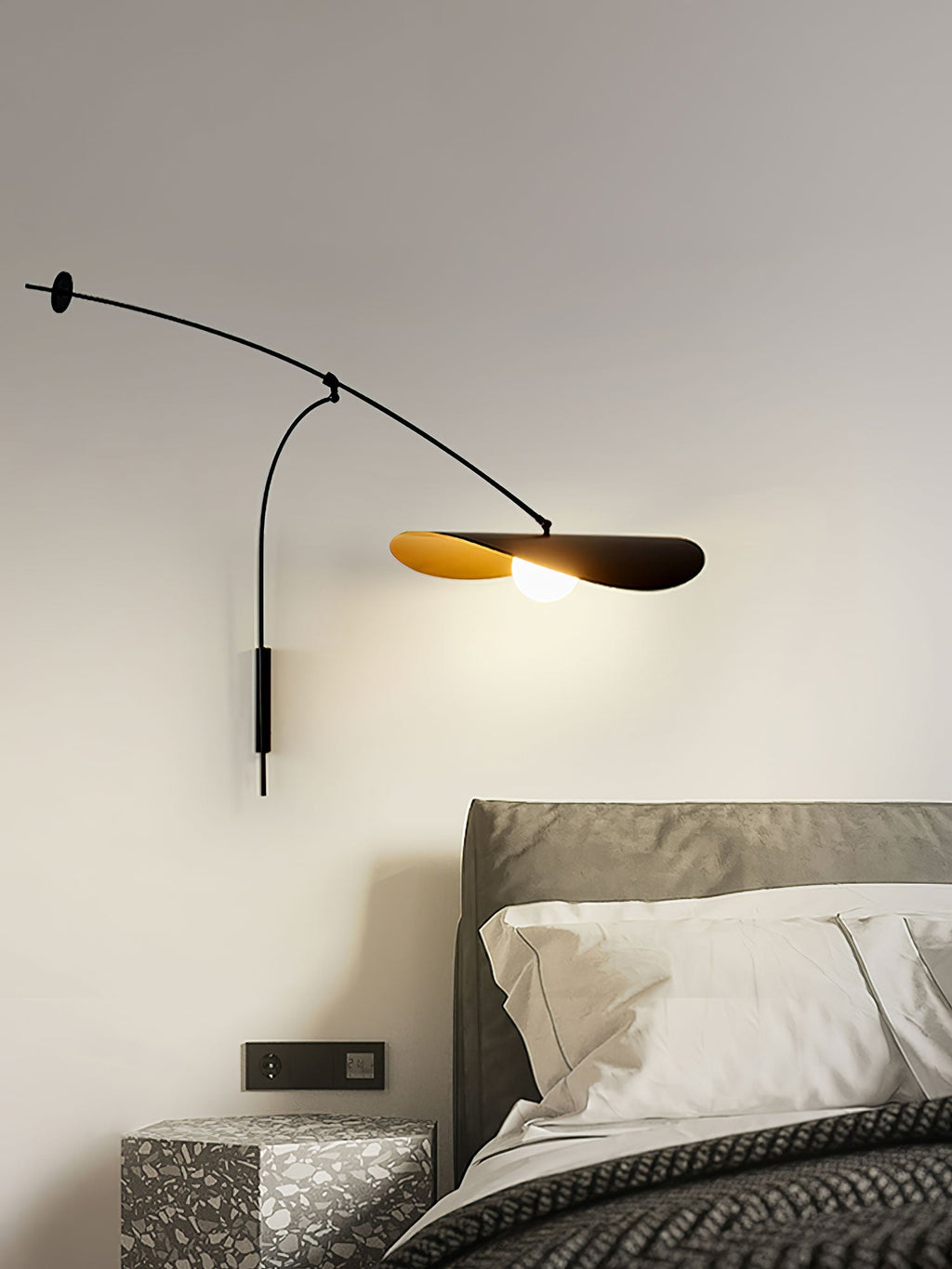 This Clérachic wall light glows over a grey headboard and white pillows, with a patterned side table at the bottom.