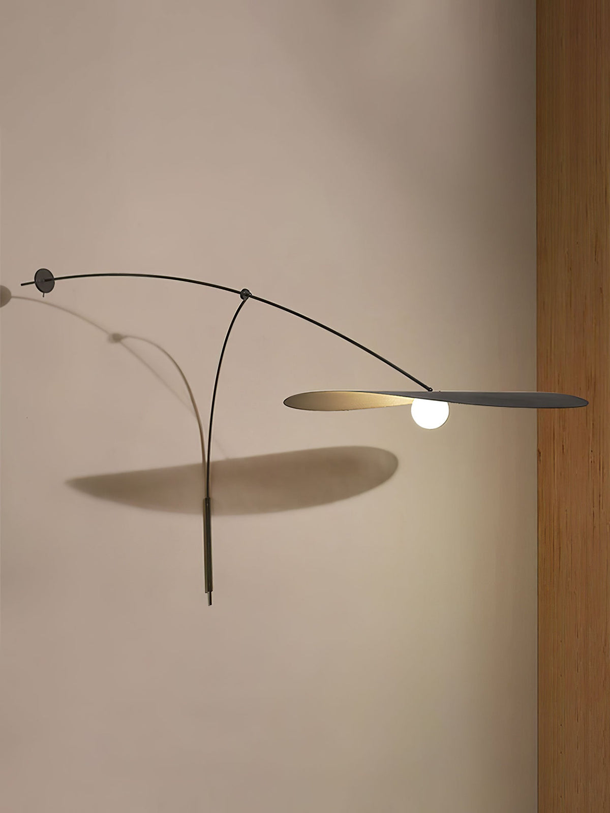 Close to a beige wall, this Clérachic wall light stretches its black shade flat and throws an angled shadow below.
