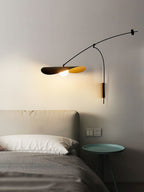 This Clérachic wall light lights a bedside corner, with a green side table, wall sockets and a grey bed below.