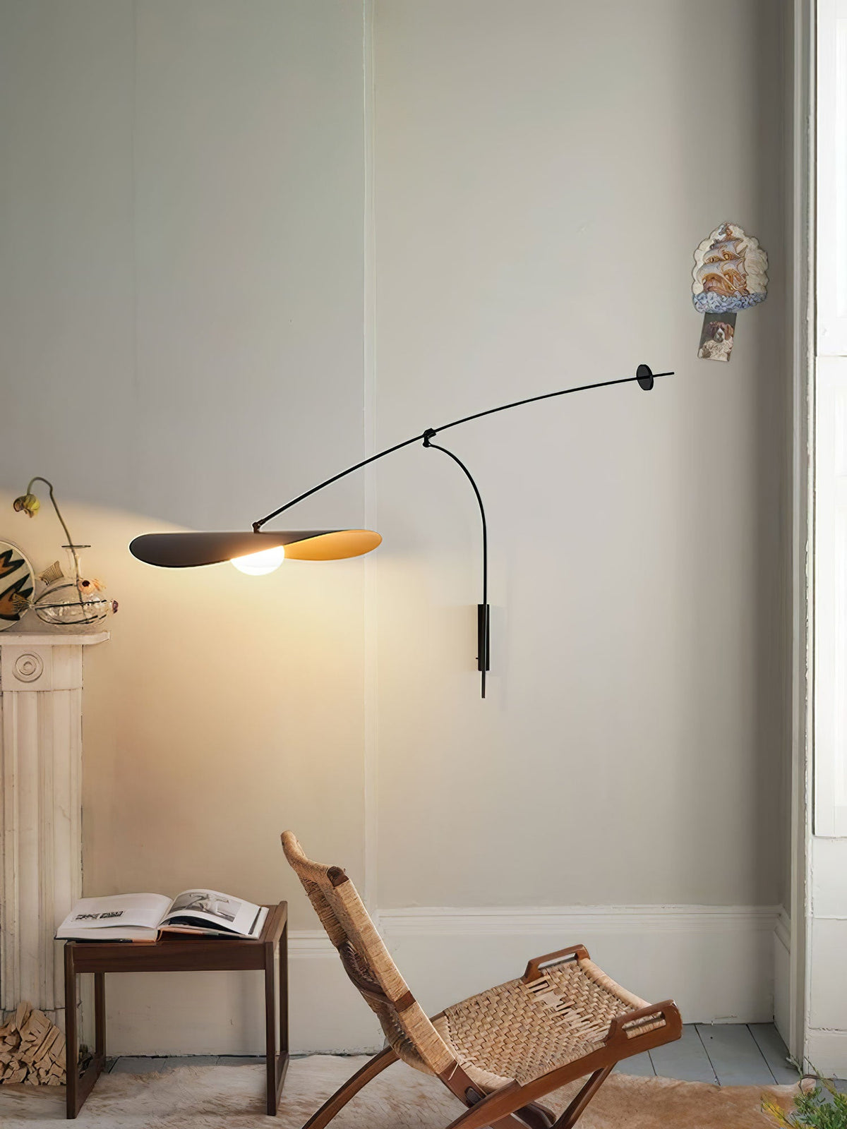 Over a wooden folding chair and a small table with an open book, this Clérachic wall light glows in a pale corner.