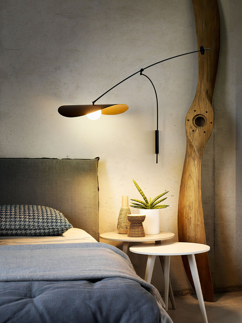 Over a bed with blue bedding and a carved wooden post, this Clérachic wall light sheds warm light from its black shade.