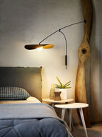Over a bed with blue bedding and a carved wooden post, this Clérachic wall light sheds warm light from its black shade.