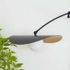 Close view of the black shade and gold-lined underside on this Clérachic wall light, with a white globe below it.