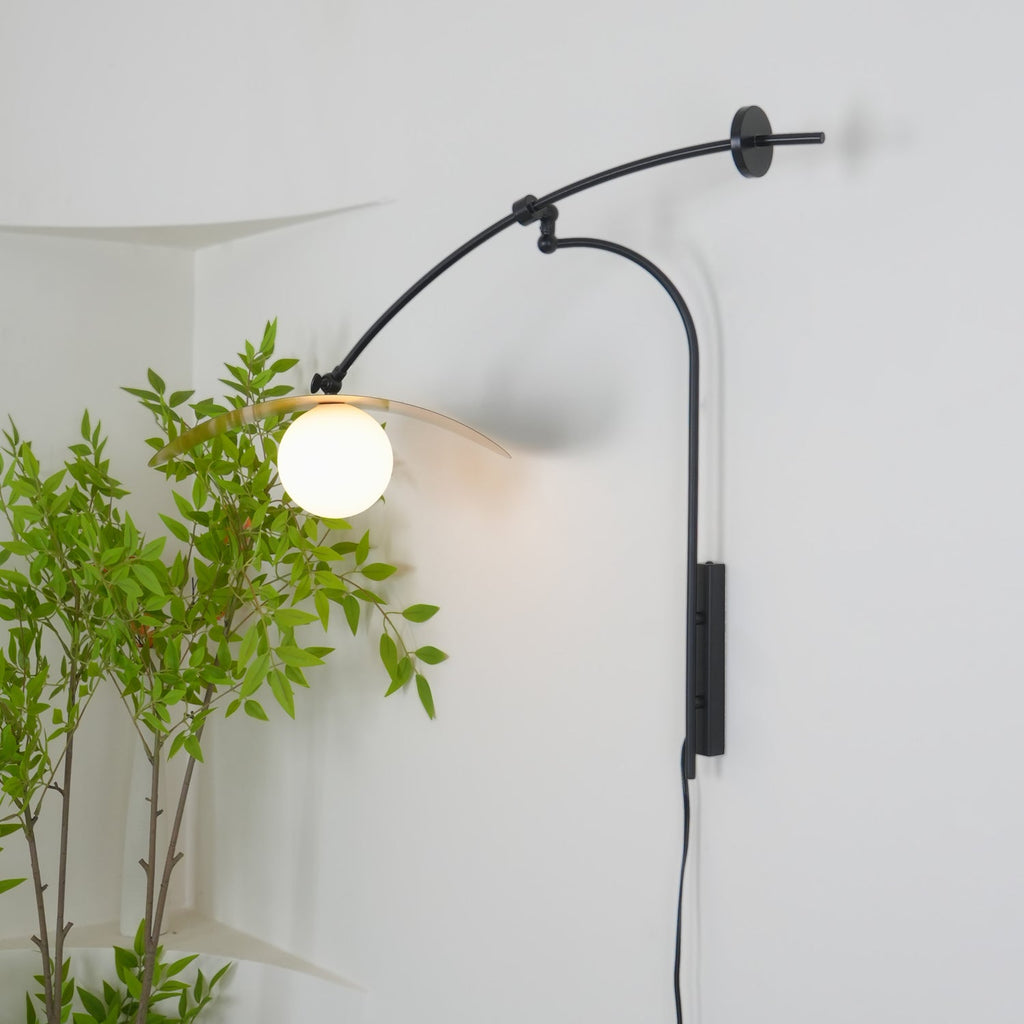 The globe of this Clérachic wall light glows warm against a white wall, with the shade tilted up behind it.