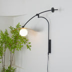 The globe of this Clérachic wall light glows warm against a white wall, with the shade tilted up behind it.