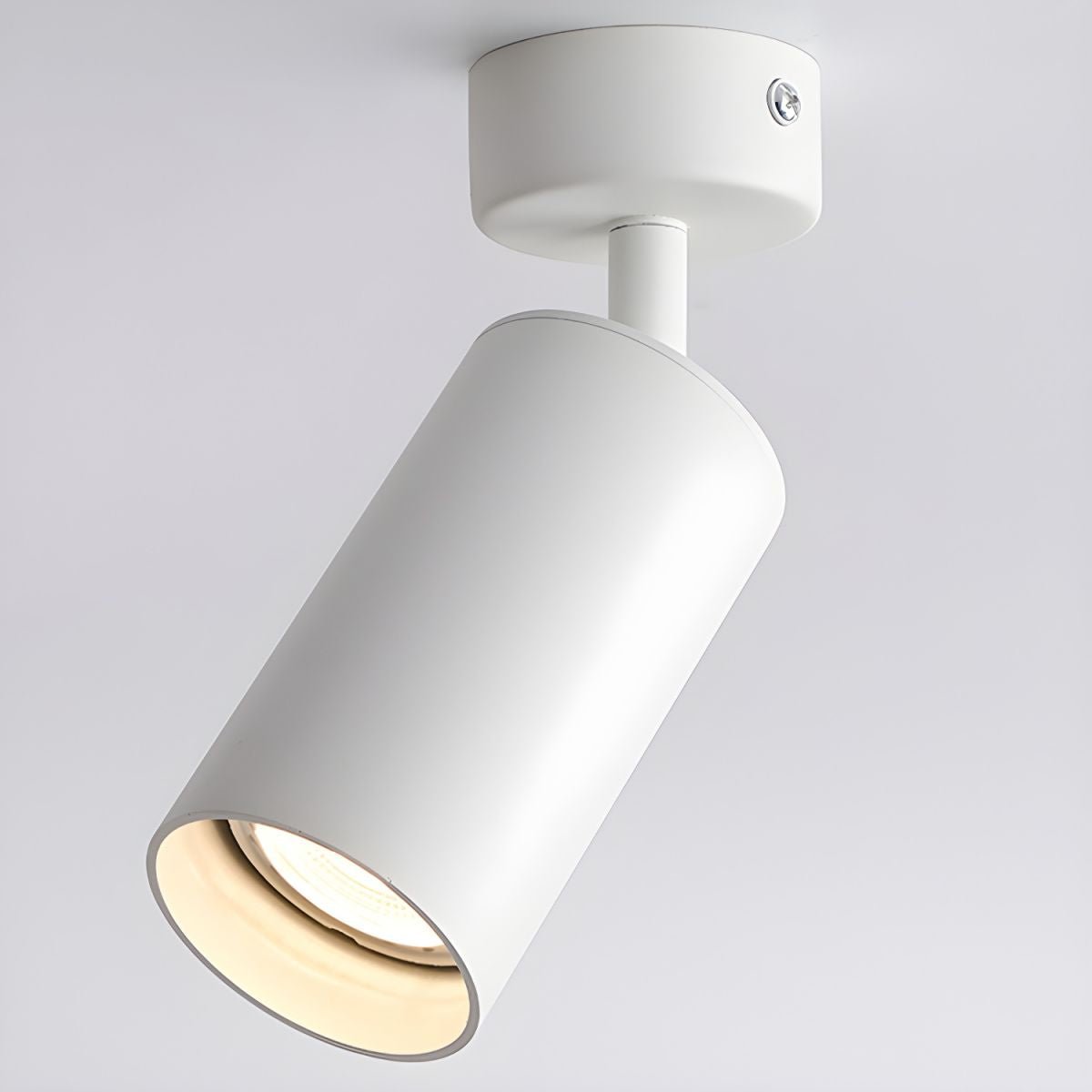 Large close-up of this Clérachic spotlight in white, the cylinder tipped on its stem and the warm bulb glowing inside the rim.