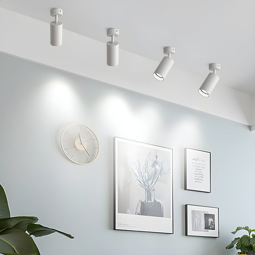 Four white Clérachic spotlights along a ceiling edge, aimed at a wall with a round clock and framed prints in a pale blue room.