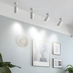 Four white Clérachic spotlights along a ceiling edge, aimed at a wall with a round clock and framed prints in a pale blue room.