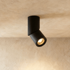 A black adjustable cylindrical downlight tilts from a plaster ceiling, its round lens lit warm, this Clérachic kitchen island fixture.