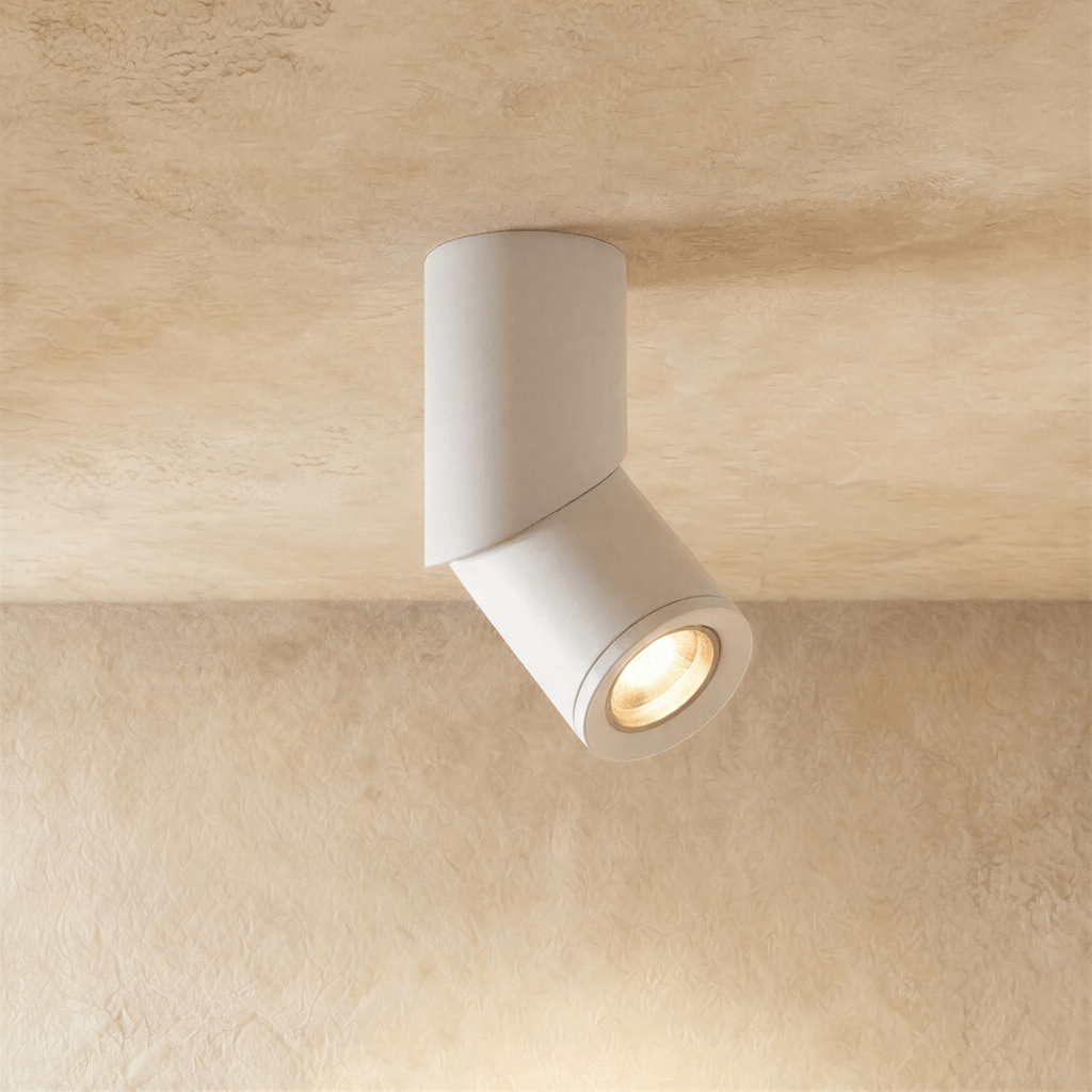 A white adjustable cylindrical downlight tilts from a plaster ceiling, its round lens lit warm, this Clérachic kitchen island fixture.