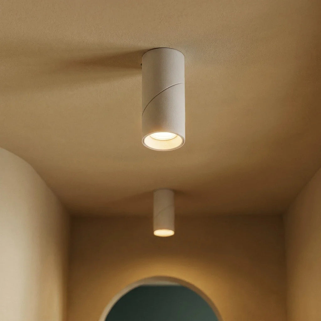Two white adjustable downlights glow along a warm hallway ceiling near an archway, these Clérachic fixtures seen close and angled.