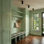 Three black adjustable downlights line a sage green mudroom ceiling above a bench and coat hooks, these Clérachic fixtures angled.