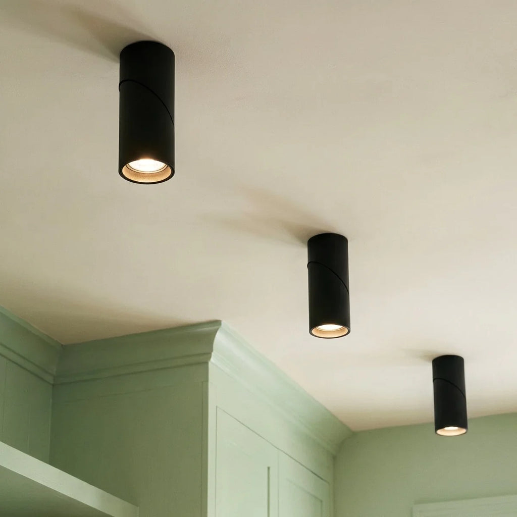 Three black adjustable downlights glow above sage green kitchen cabinetry, their lenses angled downward, Clérachic fixtures close up.