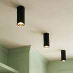 Three black adjustable downlights glow above sage green kitchen cabinetry, their lenses angled downward, Clérachic fixtures close up.