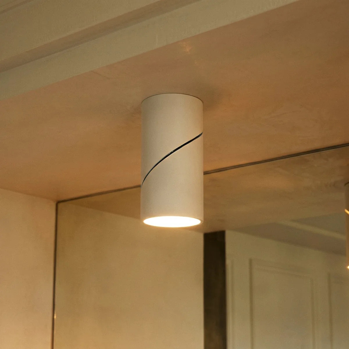 A close view of a white adjustable cylindrical downlight mounted near a mirror, its lens lit warm, this Clérachic fixture in detail.