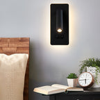 The black Clérachic reading light lit above a bedside table with a clock and small plants.