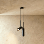 Clérachic pair of black cylinder pendants from one ceiling plate, one angled spot head and one straight, on limewash.