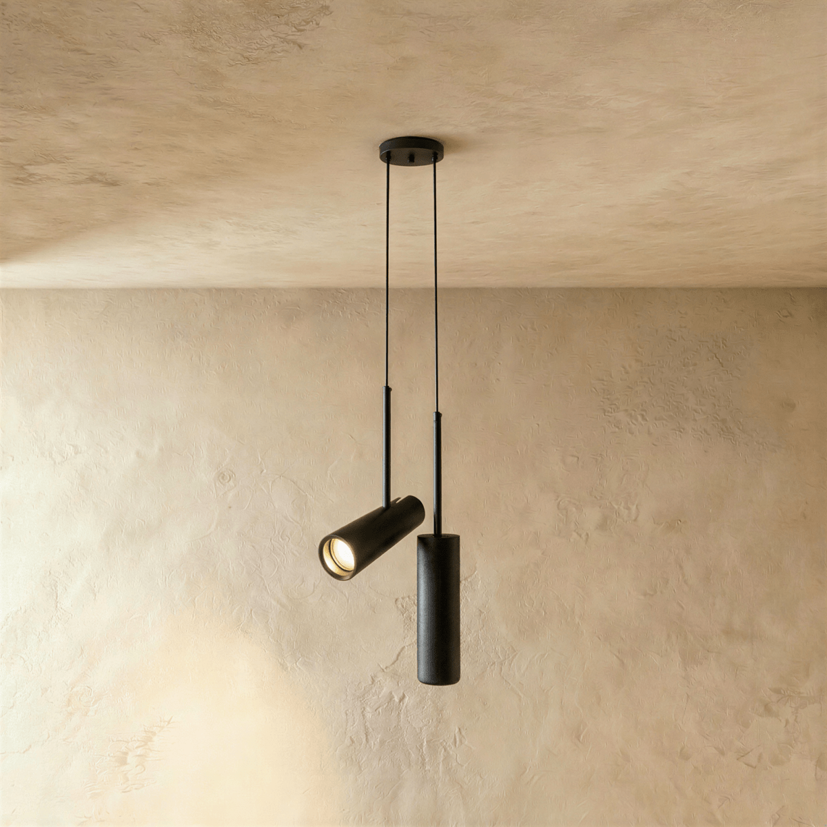 Clérachic pair of black cylinder pendants from one ceiling plate, one angled spot head and one straight, on limewash.