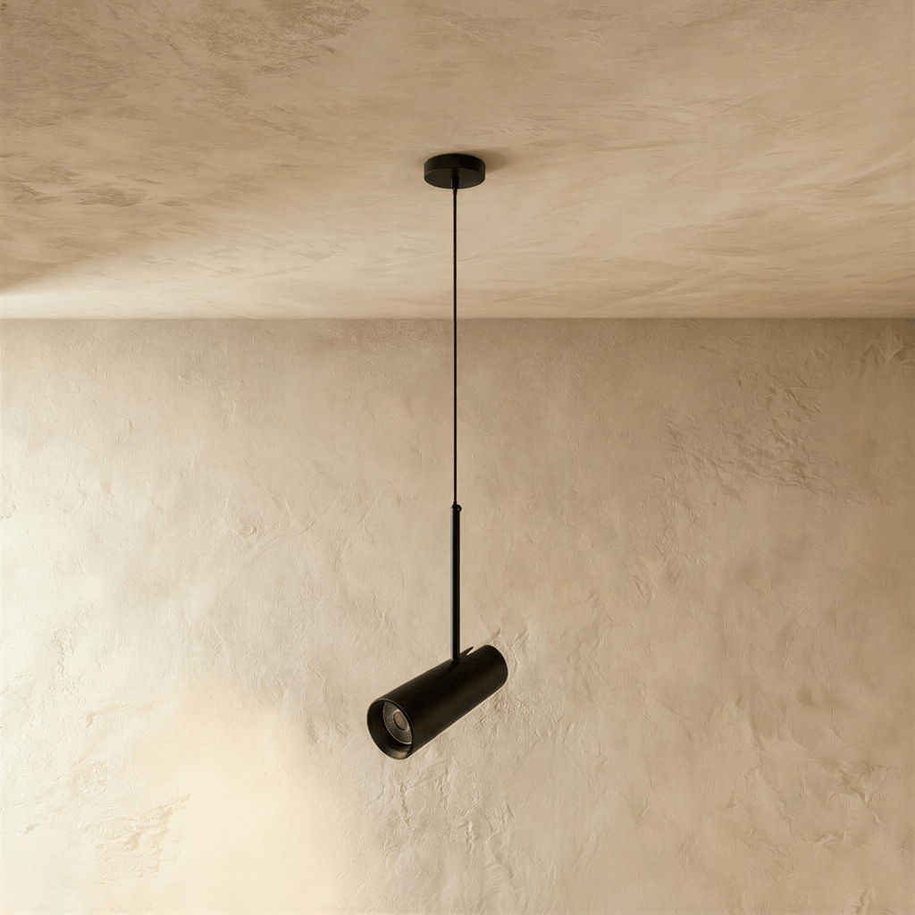 Clérachic single black cylinder pendant on a slim cord and rod, its angled head unlit, hung against a limewash wall.